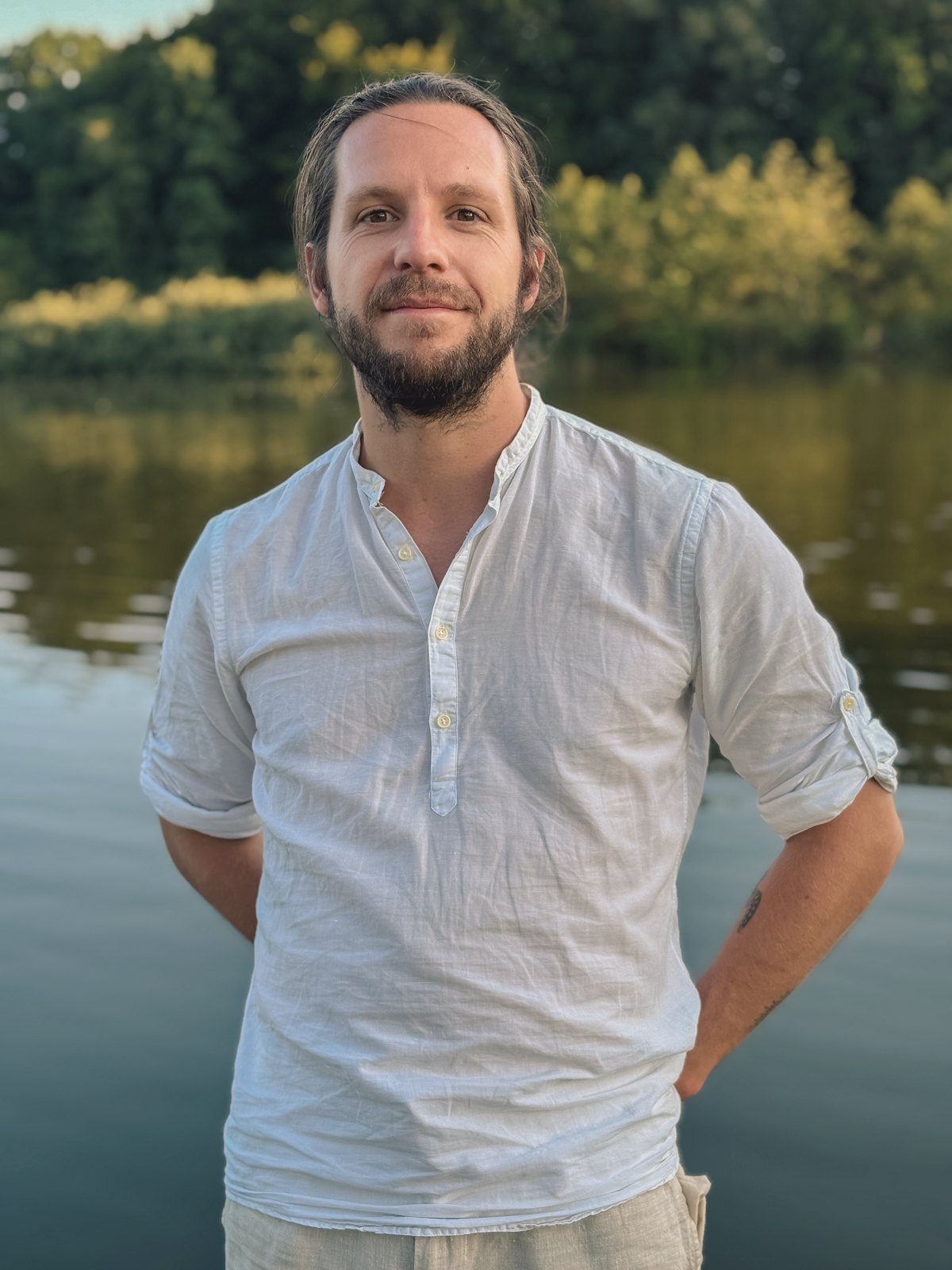 Porträt von Alexander Tautges im hellen Leinenhemd, lächelnd, im Hintergrund ein See