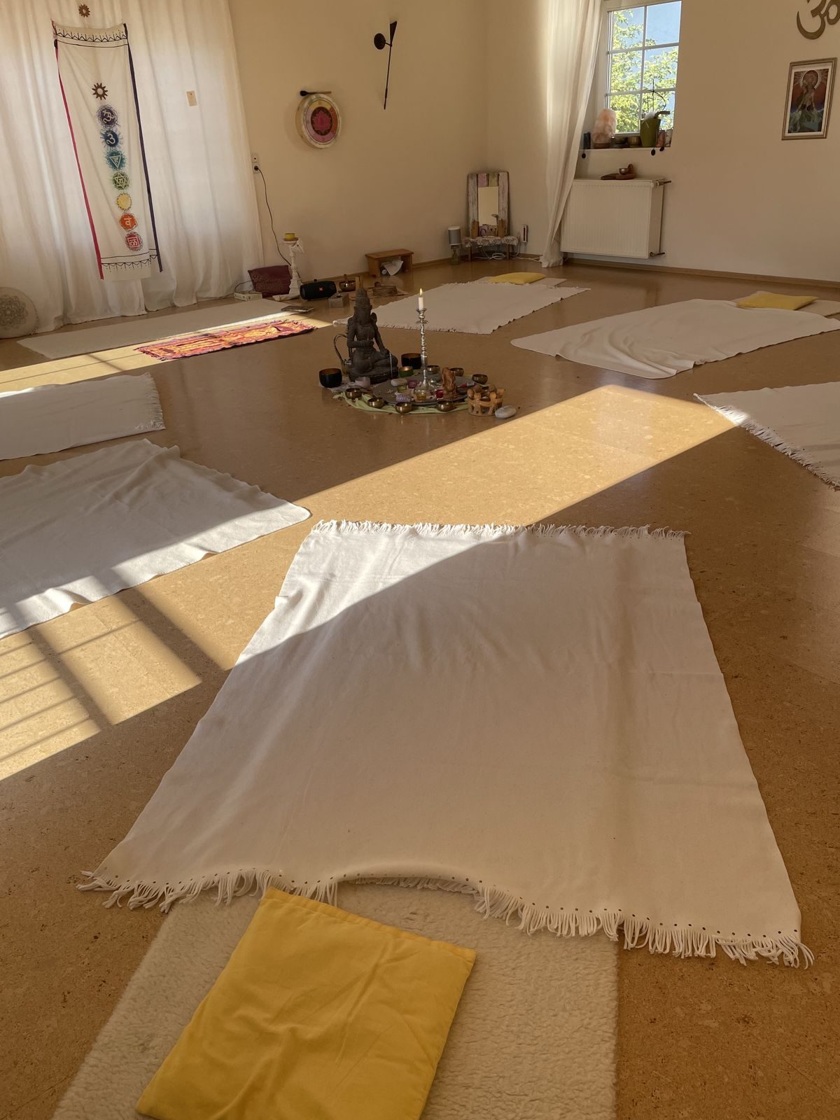 Vorbereiteter Raum für die Breathwork-Session: Decken und Kissen im Kreis, in der Mitte Kerze und Klangschalen, Sonnenlicht fällt herein